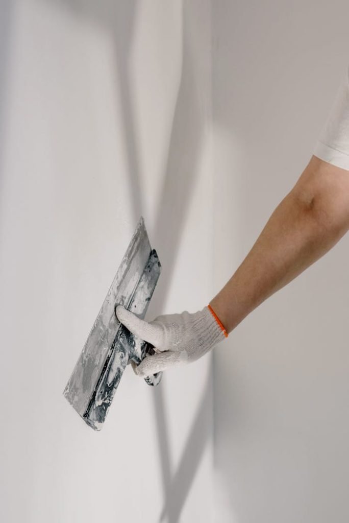 crop-man-preparing-wall-for-painting-5691622 Crop anonymous male worker in gloves holding putty knife while working at home